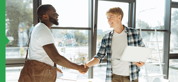 Two men shaking hands in front of an office window. Two men shaking hands in front of an office window.