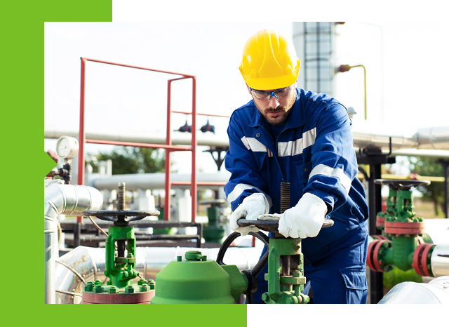 A worker in a hard hat and blue overalls doing maintenance on a gas pipeline.