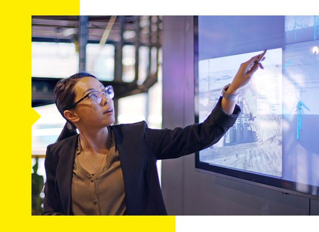 A woman points at a large screen highlighting important info.