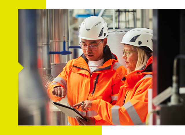 Two workers in bright orange safety gear reviewing information on a tablet.
