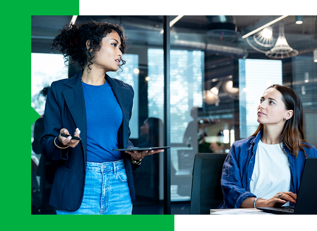 Two women in an office, one speaking while the other listens attentively.